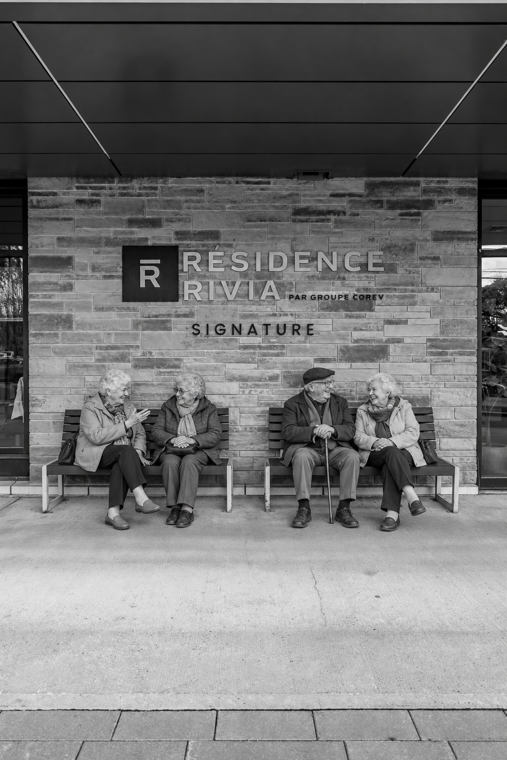 Résidents qui discutent sur les bancs devant l'entrée d'une résidence Rivia